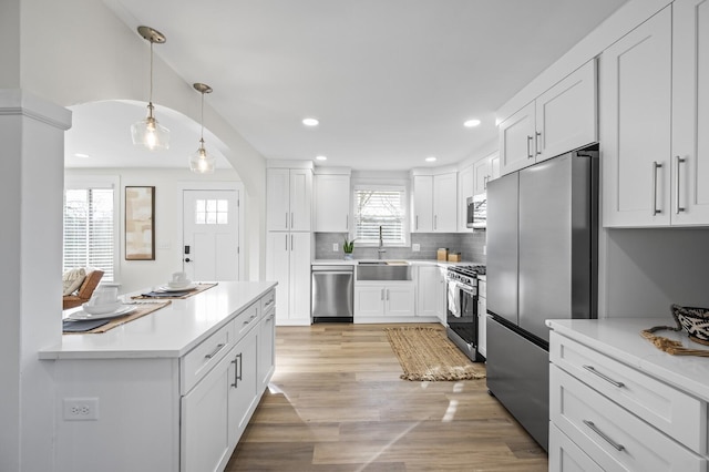 kitchen with sink, white cabinetry, stainless steel appliances, light hardwood / wood-style floors, and decorative light fixtures