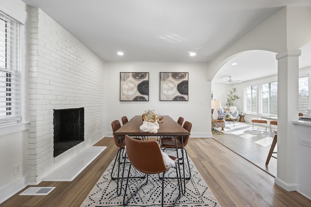 dining room featuring ceiling fan, hardwood / wood-style floors, a brick fireplace, and ornate columns