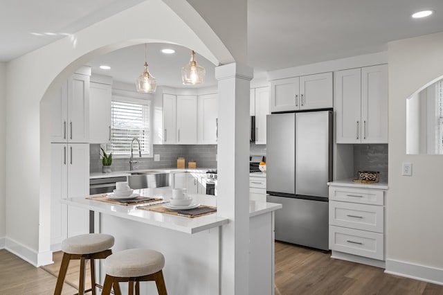 kitchen featuring stove, hanging light fixtures, stainless steel refrigerator, and white cabinets