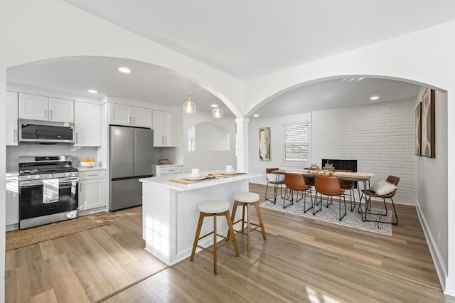 kitchen with stainless steel appliances, white cabinetry, light wood-type flooring, and decorative light fixtures