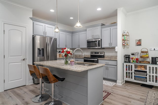 kitchen featuring pendant lighting, sink, appliances with stainless steel finishes, light stone counters, and light wood-type flooring