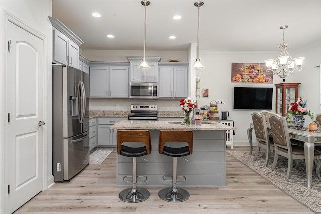 kitchen with appliances with stainless steel finishes, decorative light fixtures, an island with sink, gray cabinetry, and light stone countertops