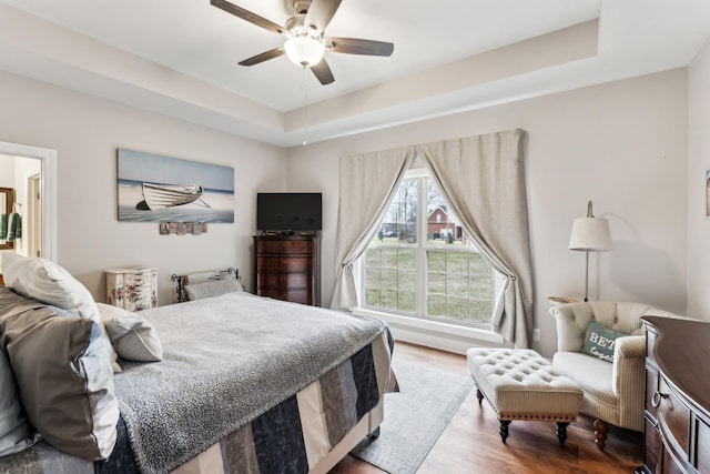 bedroom with ceiling fan, a tray ceiling, and hardwood / wood-style floors