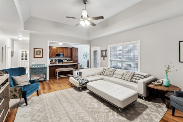 living room with ceiling fan, a raised ceiling, and light wood-type flooring