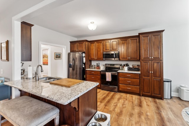 kitchen featuring sink, light wood-type flooring, kitchen peninsula, stainless steel appliances, and light stone countertops