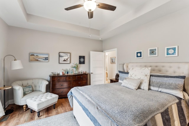 bedroom with ceiling fan, light wood-type flooring, and a tray ceiling