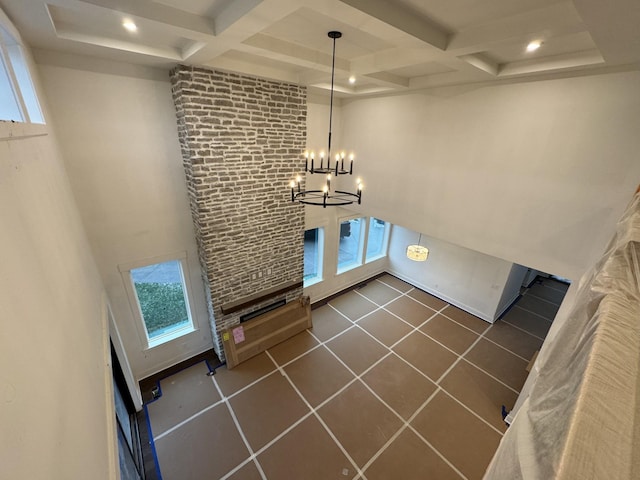 unfurnished living room with beamed ceiling, a towering ceiling, coffered ceiling, and a chandelier