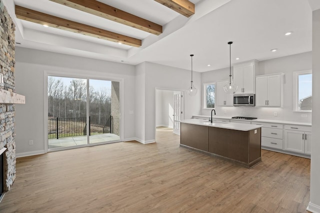 kitchen featuring sink, a stone fireplace, white cabinets, a center island with sink, and decorative light fixtures