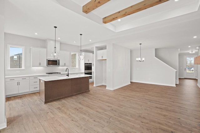 kitchen with pendant lighting, stainless steel appliances, an island with sink, and white cabinets