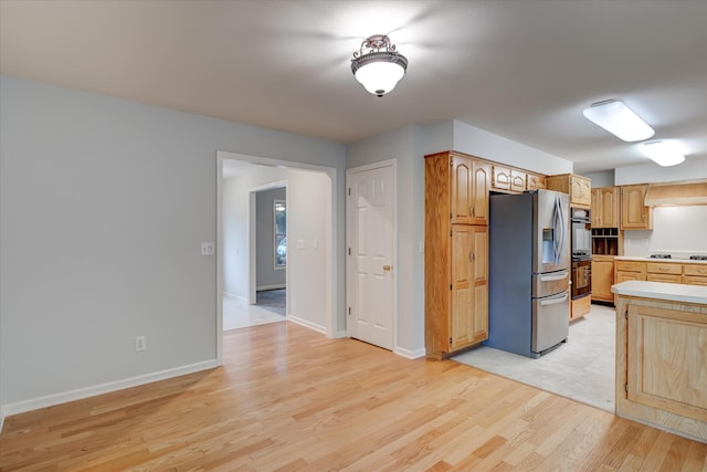 kitchen featuring stainless steel fridge, double oven, black stovetop, light wood-type flooring, and light brown cabinets