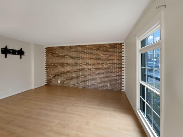 unfurnished room featuring brick wall and light hardwood / wood-style flooring