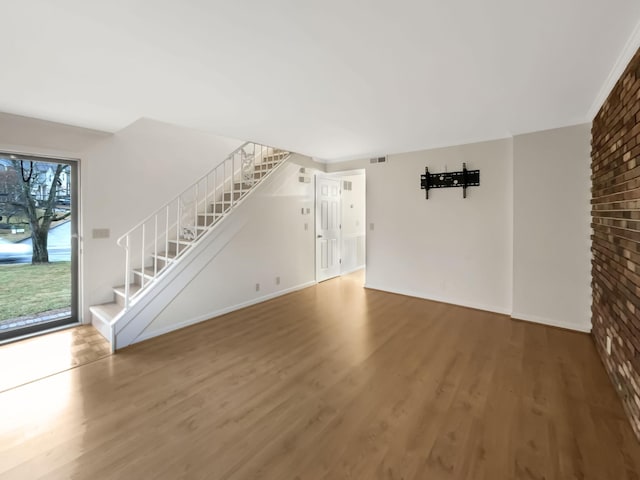 unfurnished living room with wood-type flooring and brick wall