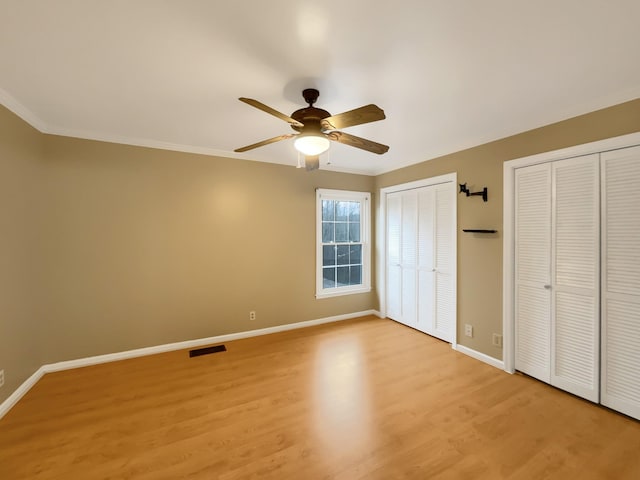 unfurnished bedroom with two closets, ornamental molding, light hardwood / wood-style floors, and ceiling fan