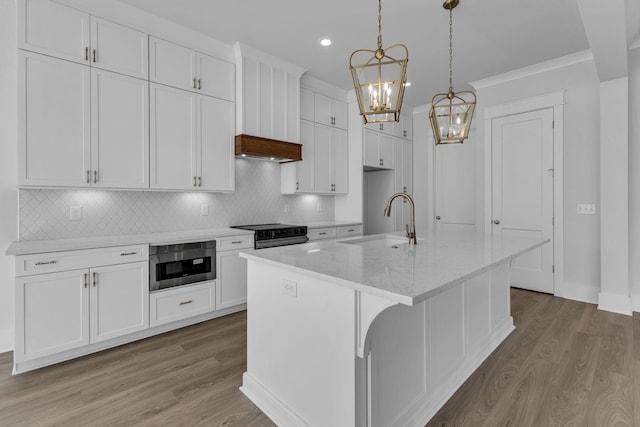 kitchen featuring pendant lighting, sink, a kitchen island with sink, light stone countertops, and white cabinets