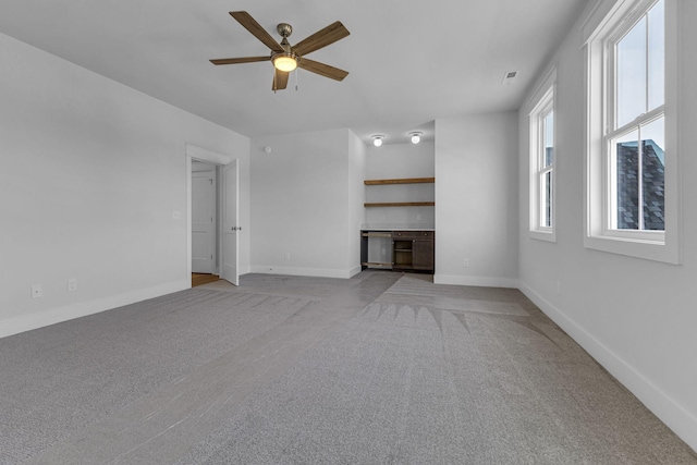 unfurnished living room featuring ceiling fan, built in desk, and light carpet