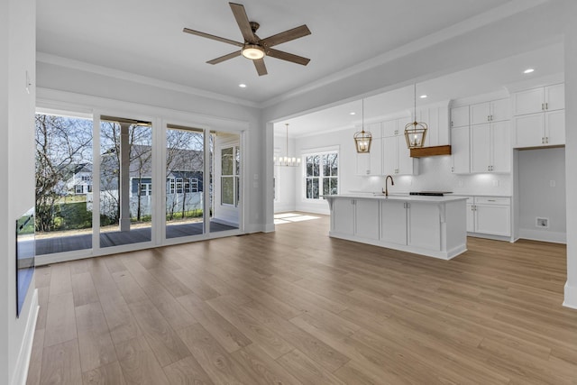 kitchen with white cabinetry, decorative light fixtures, tasteful backsplash, and a center island with sink