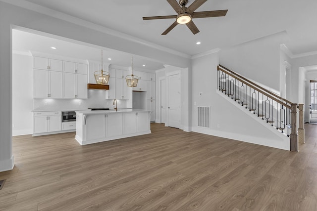 kitchen featuring pendant lighting, white cabinets, ornamental molding, a center island with sink, and light hardwood / wood-style flooring