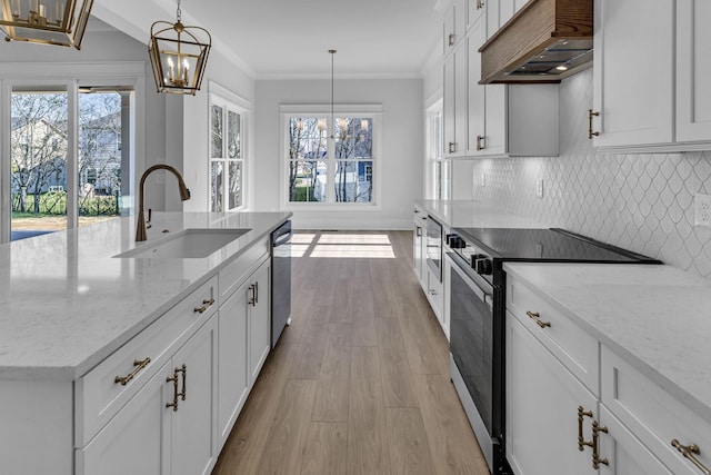 kitchen with appliances with stainless steel finishes, sink, custom exhaust hood, hanging light fixtures, and a kitchen island with sink