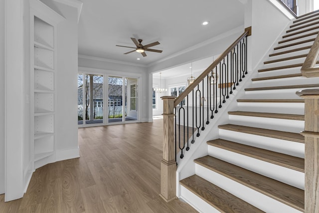 stairway with ornamental molding, ceiling fan with notable chandelier, and hardwood / wood-style floors