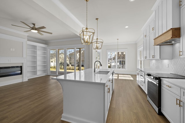 kitchen featuring sink, white cabinetry, ornamental molding, an island with sink, and decorative light fixtures