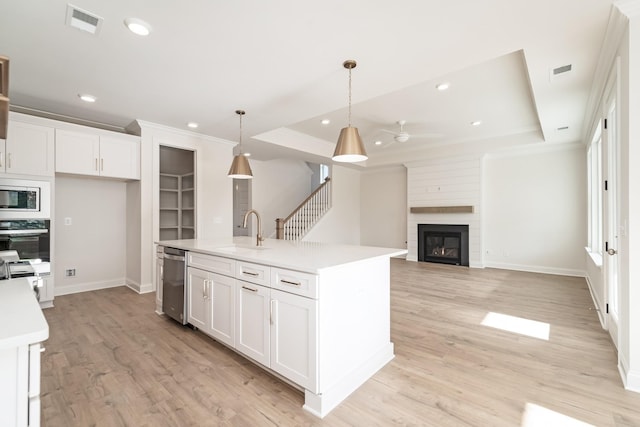 kitchen featuring a sink, light countertops, appliances with stainless steel finishes, an island with sink, and decorative light fixtures