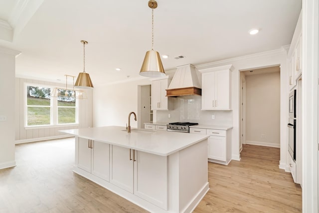 kitchen featuring stainless steel appliances, custom range hood, white cabinets, and a center island with sink