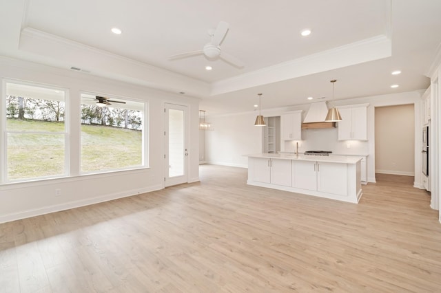 unfurnished living room with light wood-style floors, a raised ceiling, and crown molding