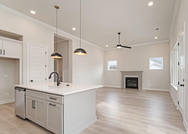 kitchen featuring sink, dishwasher, hanging light fixtures, a fireplace, and an island with sink