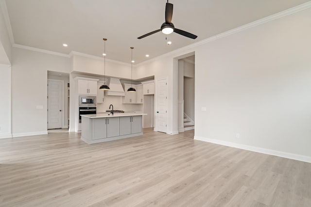 kitchen with appliances with stainless steel finishes, decorative light fixtures, an island with sink, custom exhaust hood, and light hardwood / wood-style floors