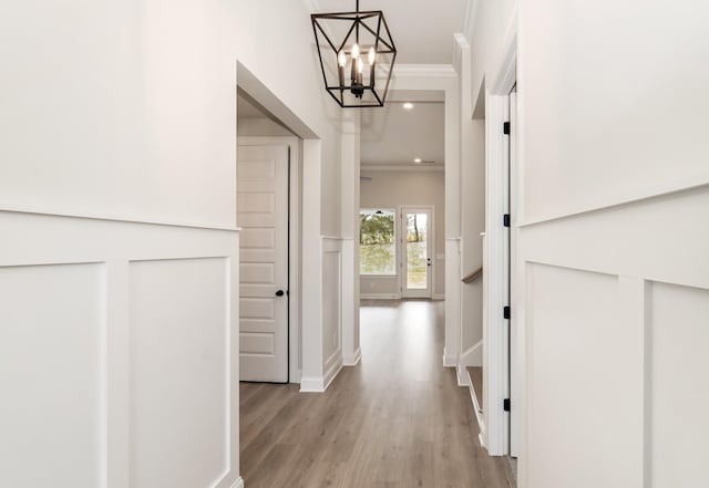 hallway with an inviting chandelier, crown molding, and light wood-type flooring