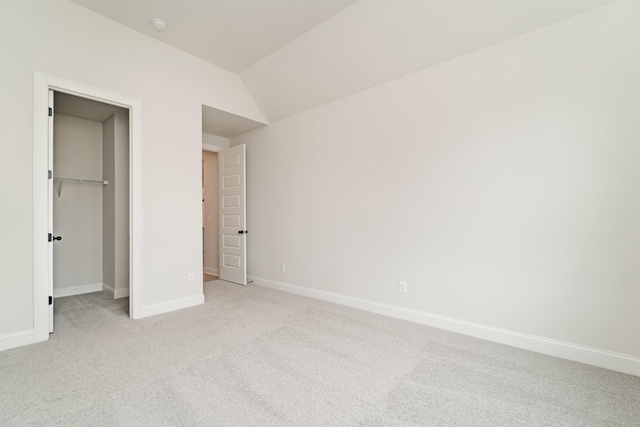 unfurnished bedroom featuring lofted ceiling, a walk in closet, light colored carpet, and baseboards