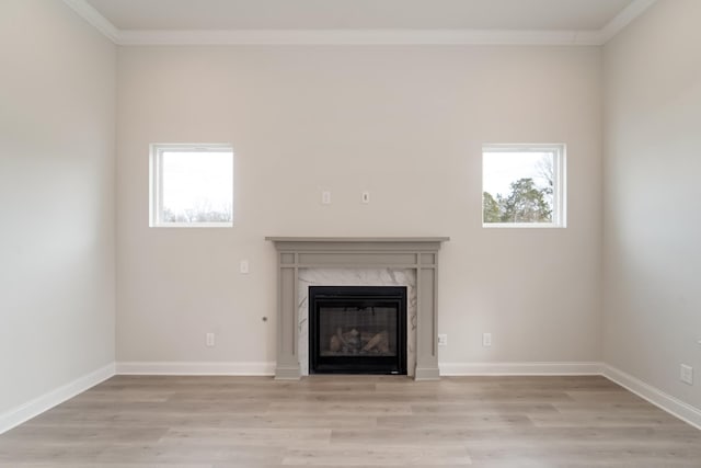 unfurnished living room with a healthy amount of sunlight, light wood-type flooring, a premium fireplace, and ornamental molding