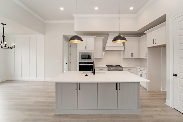 kitchen with premium range hood, appliances with stainless steel finishes, a kitchen island with sink, and white cabinets