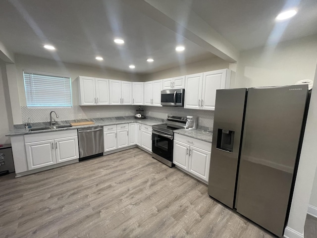 kitchen with sink, appliances with stainless steel finishes, white cabinets, light hardwood / wood-style floors, and backsplash