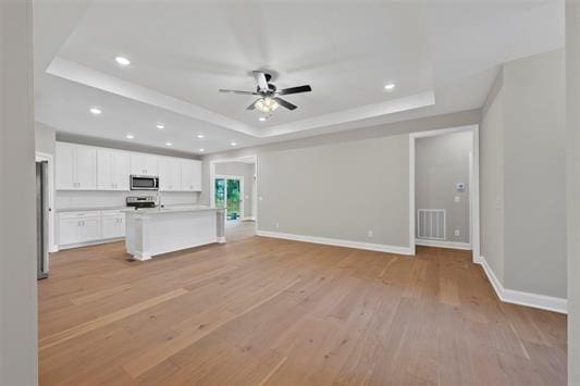 unfurnished living room featuring ceiling fan, a tray ceiling, and light wood-type flooring