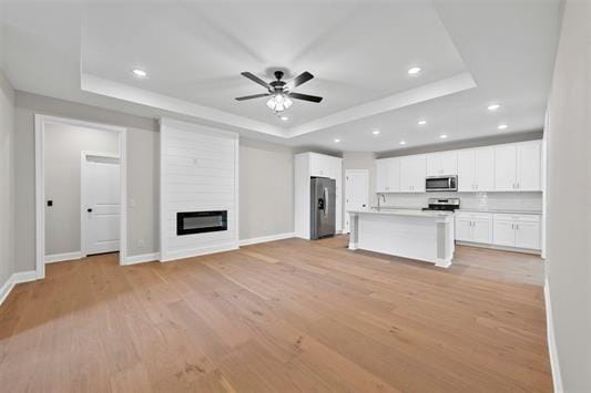 unfurnished living room featuring sink, light hardwood / wood-style flooring, ceiling fan, a fireplace, and a raised ceiling