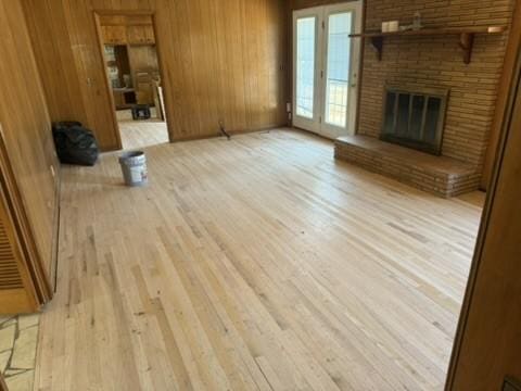 unfurnished living room featuring a fireplace, wooden walls, and light wood-type flooring