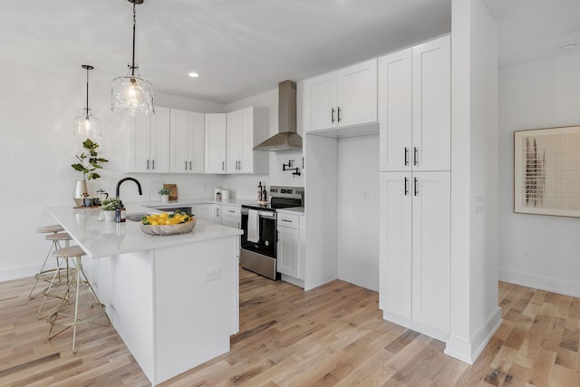 kitchen with stainless steel electric range oven, decorative light fixtures, white cabinets, a kitchen breakfast bar, and wall chimney range hood