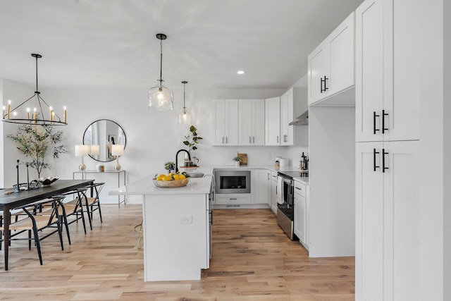 kitchen featuring white cabinetry, decorative light fixtures, light wood-type flooring, electric stove, and a kitchen island with sink