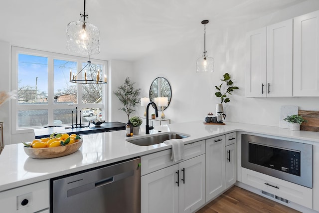 kitchen featuring built in microwave, dishwasher, white cabinetry, sink, and hanging light fixtures