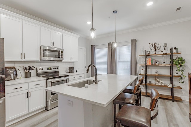 kitchen with sink, appliances with stainless steel finishes, pendant lighting, a kitchen island with sink, and white cabinets