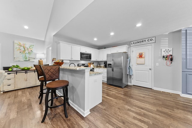 kitchen featuring hardwood / wood-style flooring, white cabinetry, stainless steel appliances, light stone counters, and a kitchen bar