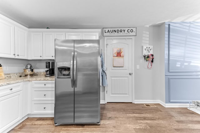 kitchen featuring light stone counters, stainless steel fridge with ice dispenser, light hardwood / wood-style flooring, and white cabinets