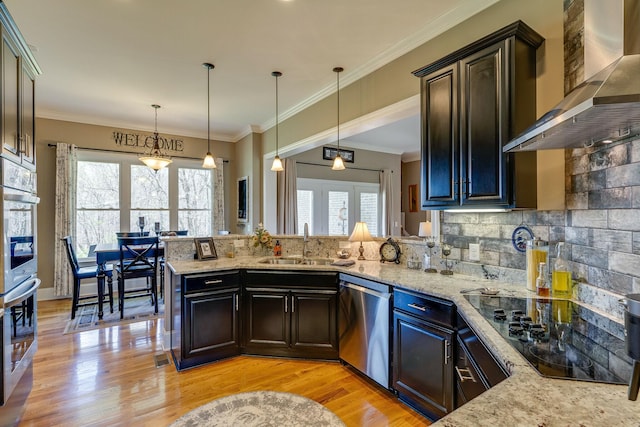 kitchen with wall chimney range hood, decorative light fixtures, sink, and appliances with stainless steel finishes