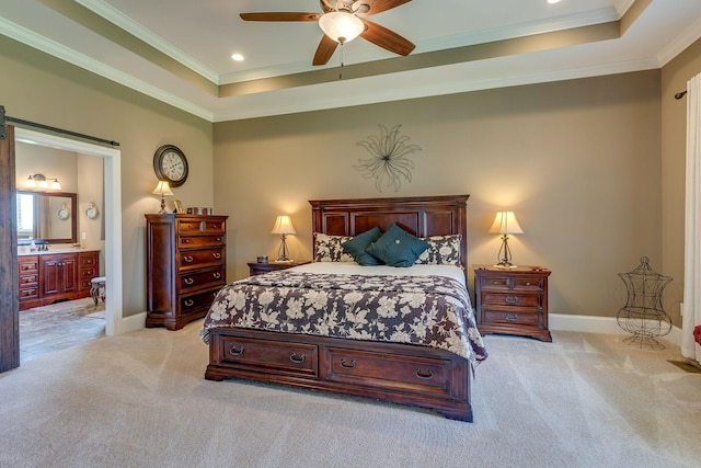 carpeted bedroom with ornamental molding, a barn door, ensuite bath, and a tray ceiling