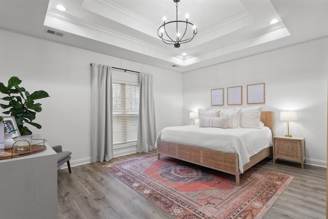 bedroom with a raised ceiling, crown molding, wood-type flooring, and a chandelier