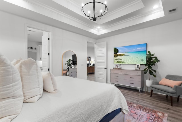 bedroom with crown molding, dark wood-type flooring, ensuite bath, a raised ceiling, and a chandelier