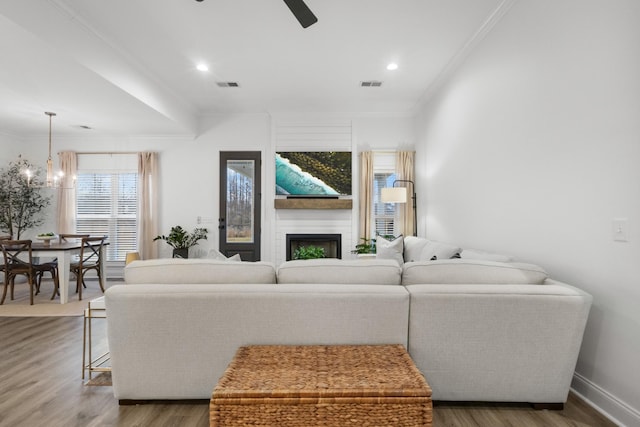 living room with crown molding, a fireplace, ceiling fan with notable chandelier, and hardwood / wood-style flooring