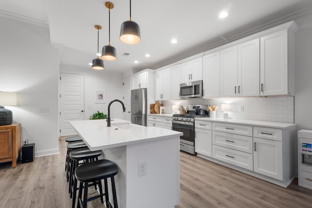 kitchen with pendant lighting, appliances with stainless steel finishes, a center island with sink, and white cabinets