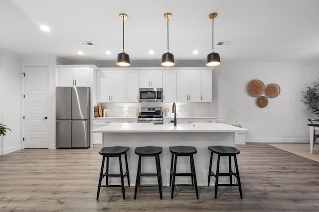 kitchen with sink, hanging light fixtures, a center island with sink, stainless steel appliances, and white cabinets